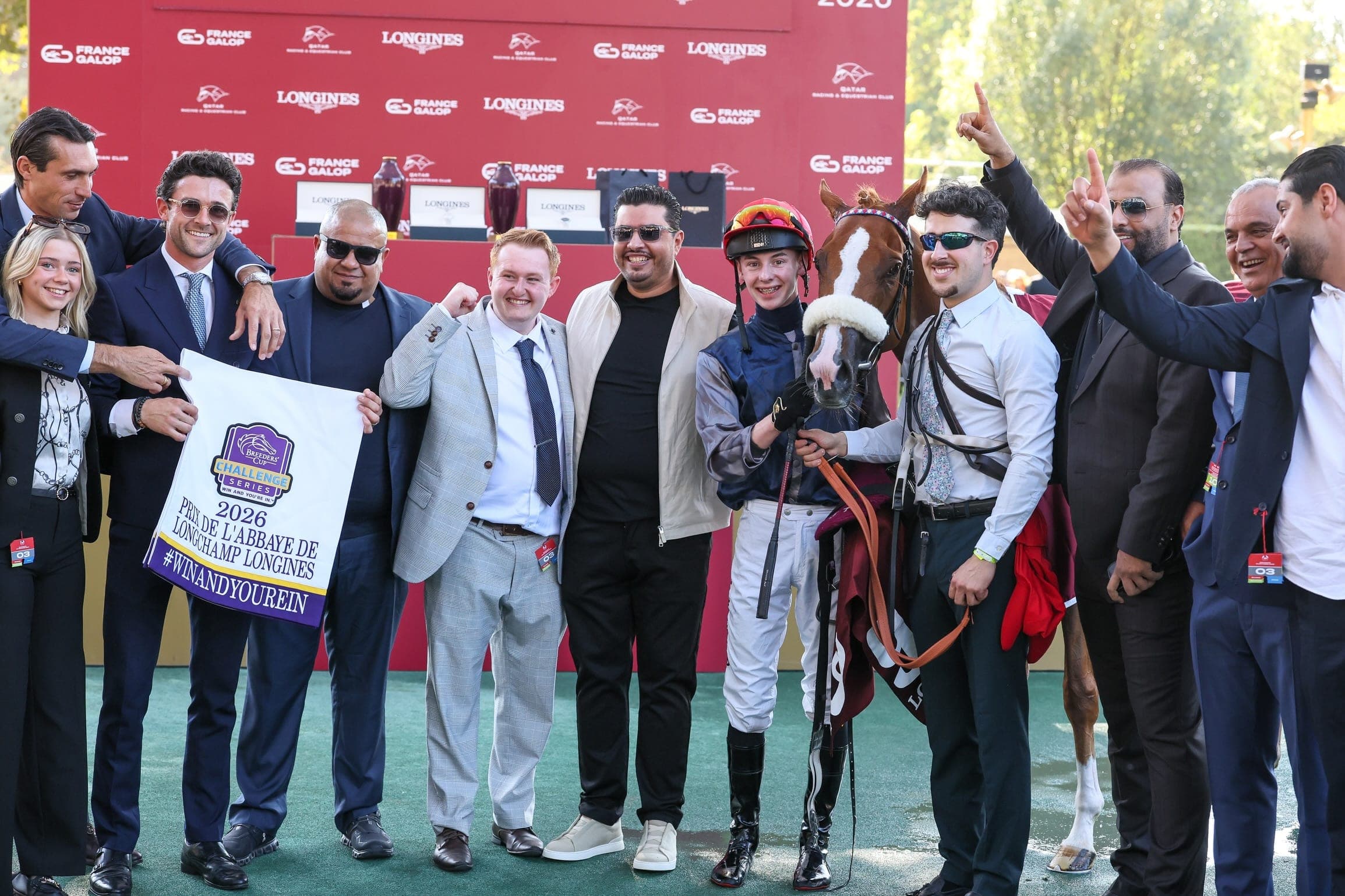 Miss Yechance's team and jockey Jack Nicholls celebrate in the winner's enclosure with a Prix de l'Abbaye de Longchamp 2026 banner